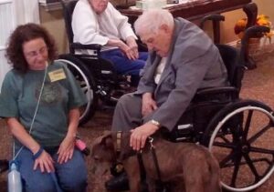 Man in wheelchair petting brown dog at Animal Welfare Association Pet Therapy session.