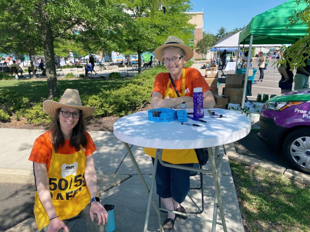 2 volunteers standing at table at AWA Paws & Feet 2022.