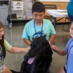 three children petting black dog at Animal Welfare Associations Kids Camp.