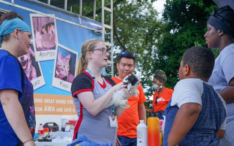 Veterinarian holding dog speaking with family at Animal Welfare Association Vets on Wheels.