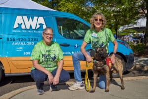 Two women in green shirts posing with shepherd dog in front of AWA Van.