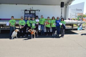 Group of women in green shirts with 2 dogs posing at Paws & Feet stage.
