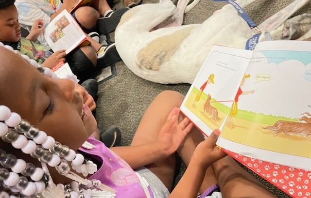 Young student reading book accompanied by therapy dog at AWA Compassionate Kids Reading Program event.