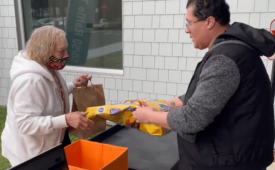 Woman in white jacket receiving donated pet food from man at Animal Welfare Association's Pet Food Pantry.