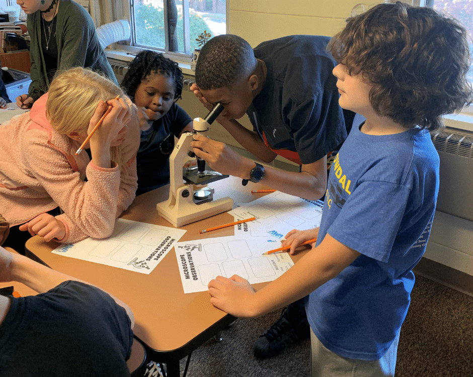 Elementary aged kids looking through microscopes and working on worksheets