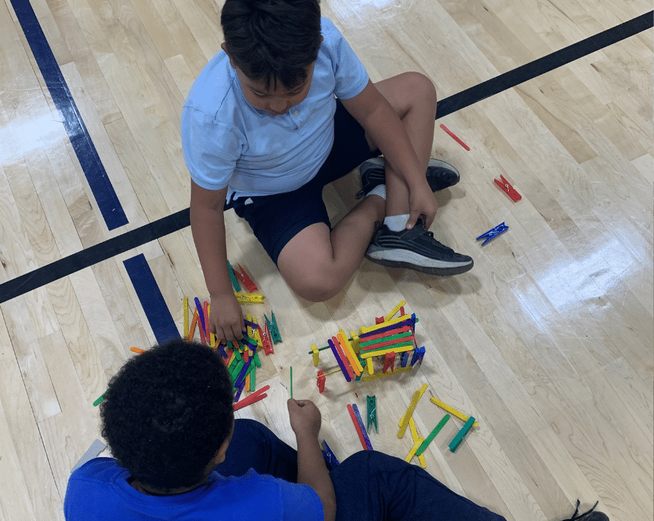 Two elementary aged boys building with popsicle sticks on a floor