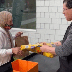 Woman wearing a mask receiving a bag of dog food from a man in a gray shirt