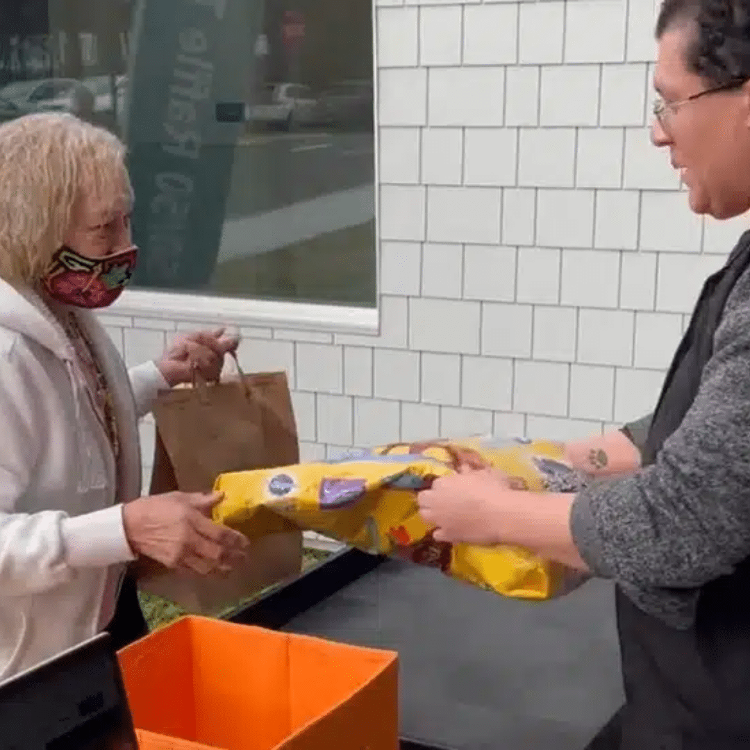 Woman wearing a mask receiving a bag of dog food from a man in a gray shirt