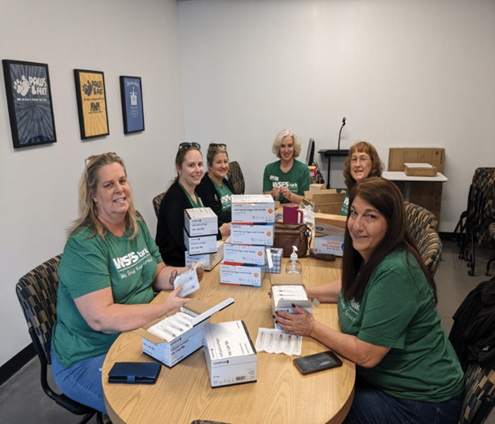 WSFS Bank volunteers wearing green tshirts sitting around a long table full of white boxes.