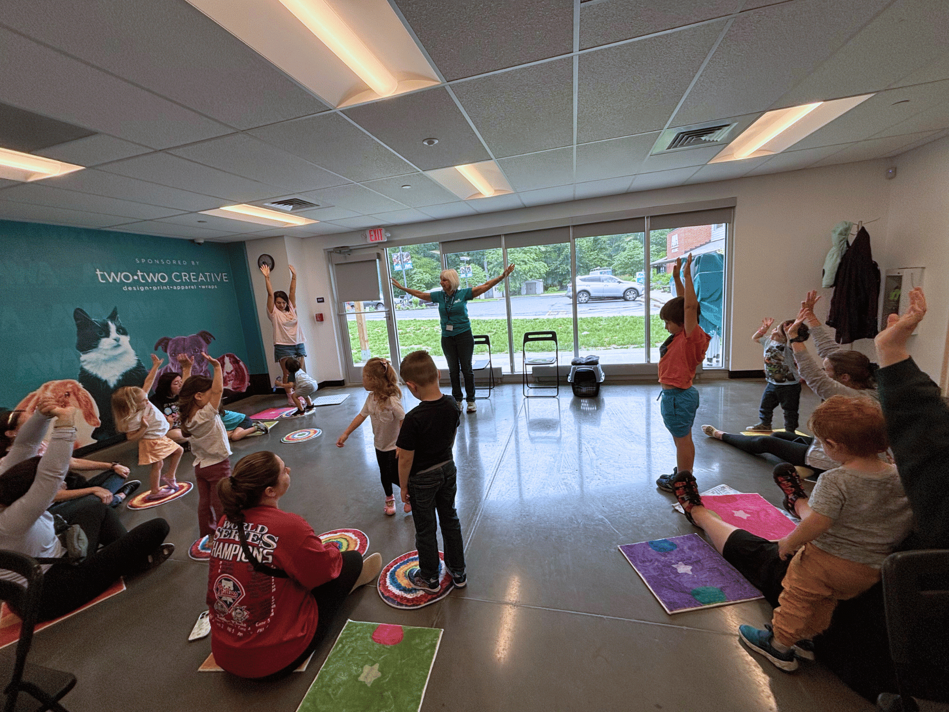 A group of children and their parents participating in a movement exercise being taught by an instructor