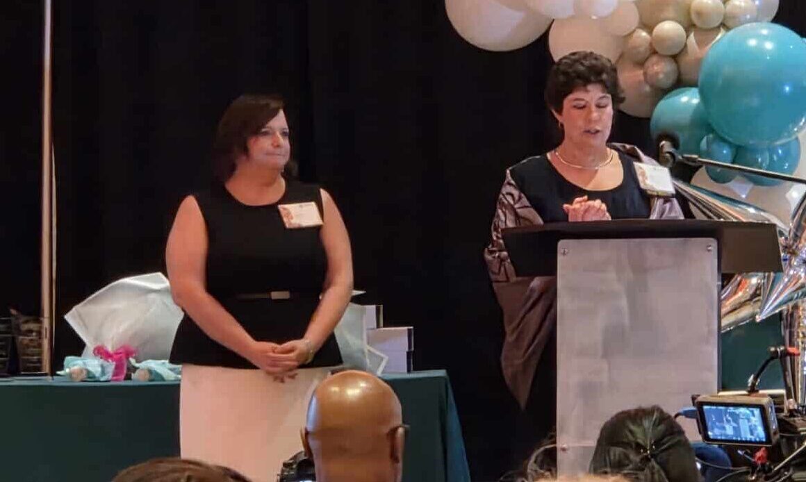 Executive Director Laura Houston receiving accolades below a teal and white balloon arch.
