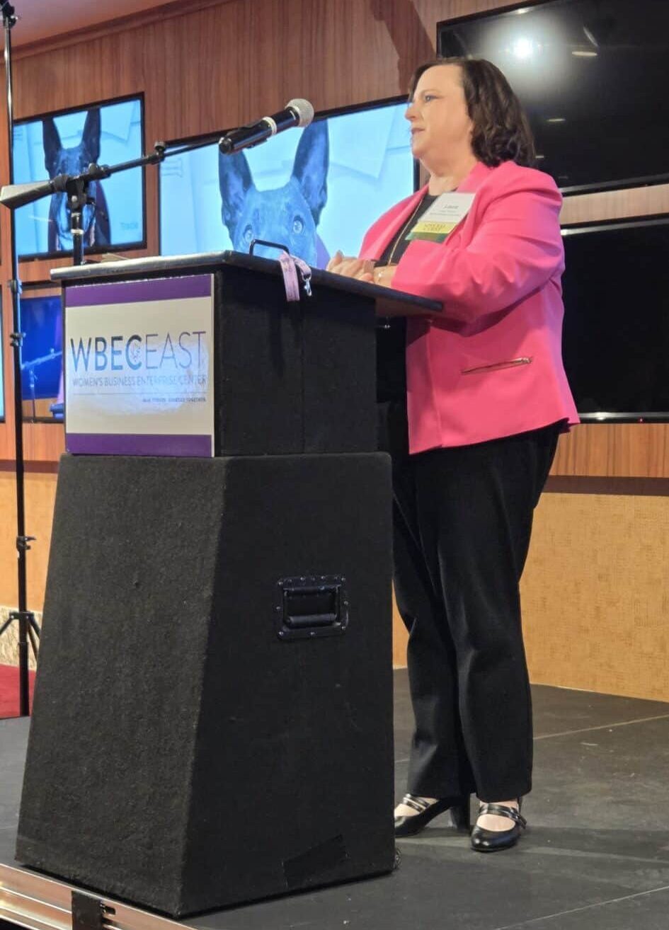 Executive Director Laura Houston speaking behind a lectern at the WBEC East conference